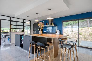 Cette image montre une grande cuisine ouverte parallèle et encastrable rustique avec un plan de travail en bois, une crédence bleue, une crédence en feuille de verre et îlot.