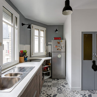 Cette image montre une cuisine linéaire design fermée et de taille moyenne avec un évier 2 bacs, un placard à porte plane, des portes de placard en bois brun, aucun îlot, un plan de travail en stratifié, une crédence blanche, une crédence en fenêtre, un électroménager en acier inoxydable, un sol en carreaux de ciment, un sol gris et un plan de travail blanc.