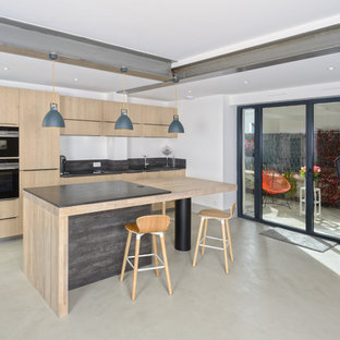 Inspiration pour une cuisine design avec un placard à porte plane, des portes de placard en bois clair, un électroménager noir, un îlot central et un sol beige.