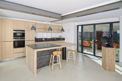 Inspiration pour une cuisine design en bois clair avec un placard à porte plane, un électroménager noir, îlot et un sol beige.