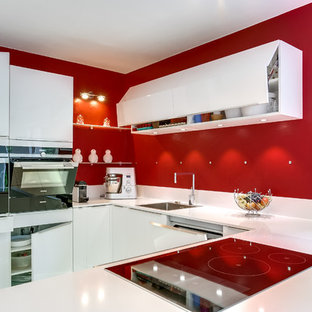 Cette photo montre une cuisine américaine tendance en U de taille moyenne avec un évier encastré, un placard à porte plane, des portes de placard blanches, une crédence rose et un électroménager blanc.