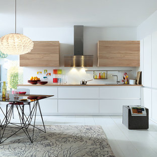 Idée de décoration pour une cuisine américaine design avec un évier posé, un placard à porte plane, des portes de placard blanches, un électroménager en acier inoxydable, un sol en bois peint, aucun îlot et un sol blanc.