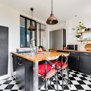 Idées déco pour une cuisine parallèle industrielle fermée et de taille moyenne avec un évier 2 bacs, des portes de placard noires, un plan de travail en bois, une crédence blanche, une péninsule, un placard à porte shaker, une crédence en carrelage métro, un électroménager en acier inoxydable, un sol en carrelage de céramique, un sol noir et un plan de travail marron.