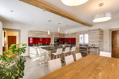 Bild på ett stort funkis kök, med en undermonterad diskho, släta luckor, skåp i ljust trä, bänkskiva i kvartsit, rött stänkskydd, glaspanel som stänkskydd, rostfria vitvaror, skiffergolv och en köksö