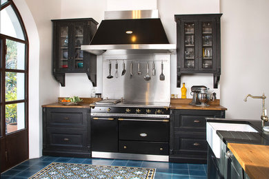 Idéer för vintage brunt kök, med en rustik diskho, luckor med upphöjd panel, svarta skåp, träbänkskiva, stänkskydd med metallisk yta, svarta vitvaror och blått golv