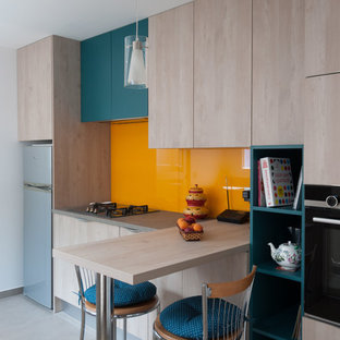 Exemple d'une cuisine parallèle tendance fermée et de taille moyenne avec un évier intégré, un placard à porte affleurante, des portes de placard en bois clair, un plan de travail en stratifié, une crédence orange, une crédence en feuille de verre, un électroménager en acier inoxydable, un sol en carrelage de céramique, aucun îlot, un sol gris et un plan de travail gris.