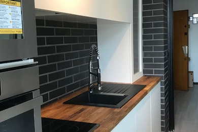 Small contemporary galley enclosed kitchen in Reims with a single-bowl sink, white cabinets, wood worktops, black splashback, brick splashback, stainless steel appliances and no island.