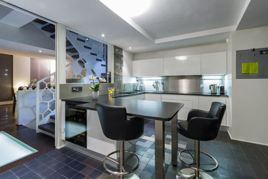 Cette image montre une grande cuisine ouverte design en U avec un placard à porte plane, des portes de placard blanches, une crédence métallisée et une péninsule.
