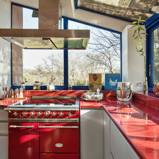 This is an example of a large midcentury galley eat-in kitchen in Marseille with a double-bowl sink, flat-panel cabinets, grey cabinets, solid surface benchtops, red splashback, panelled appliances, medium hardwood floors, with island, brown floor and red benchtop.