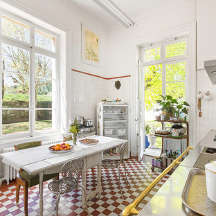 Réalisation d'une cuisine américaine linéaire champêtre avec un évier 2 bacs, un plan de travail en inox, une crédence blanche, un sol rouge et un plan de travail gris.