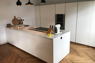 Inspiration for a large contemporary galley light wood floor open concept kitchen remodel in Paris with an undermount sink, flat-panel cabinets, white cabinets, quartzite countertops, black appliances, an island and white countertops