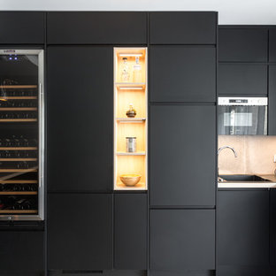 Réalisation d'une cuisine nordique en L avec un évier 1 bac, un placard à porte plane, des portes de placard noires, une crédence grise, un électroménager encastrable, une péninsule et un plan de travail gris.
