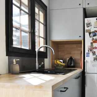 Design ideas for a mid-sized scandinavian u-shaped open plan kitchen in Lille with an undermount sink, flat-panel cabinets, wood benchtops, black splashback, glass sheet splashback, black appliances, terra-cotta floors, with island and grey floor.