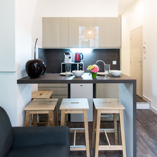 Réalisation d'une cuisine ouverte linéaire design avec un placard à porte plane, des portes de placard beiges, une crédence noire, un électroménager blanc, un sol en bois foncé, aucun îlot, un sol marron et un plan de travail noir.