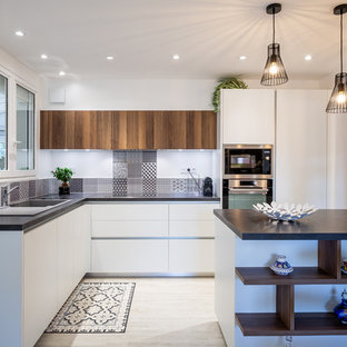 Idée de décoration pour une cuisine nordique en L de taille moyenne avec un placard à porte plane, des portes de placard blanches, une crédence multicolore, une crédence en carreau de ciment, un électroménager noir, un îlot central, un sol beige et un plan de travail noir.