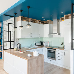Idées déco pour une cuisine contemporaine avec un évier posé, un placard à porte plane, des portes de placard blanches, un plan de travail en bois, une crédence verte, une crédence en feuille de verre, un électroménager en acier inoxydable, un sol en bois clair, une péninsule, un sol beige et un plan de travail beige.