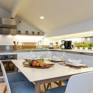 Inspiration pour une cuisine américaine marine en L avec un placard à porte plane, des portes de placard blanches, une crédence en carreau de miroir, un électroménager en acier inoxydable, un sol en bois clair, aucun îlot et un sol beige.