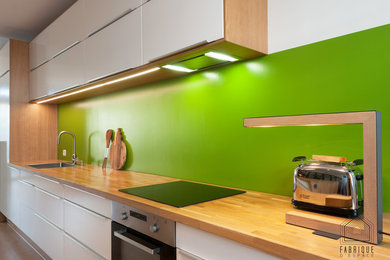 Exemple d'une grande cuisine ouverte linéaire scandinave avec un évier 1 bac, un placard à porte plane, des portes de placard blanches, un plan de travail en bois, une crédence verte, un électroménager en acier inoxydable, parquet clair et îlot.