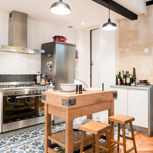 Photo of a mid-sized industrial galley eat-in kitchen in Bordeaux with zinc benchtops, black splashback, stainless steel appliances, ceramic floors, white cabinets and with island.
