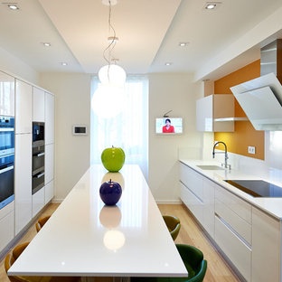Inspiration pour une cuisine parallèle design avec un évier encastré, un placard à porte plane, des portes de placard blanches, une crédence jaune, un électroménager noir, un sol en bois clair, un îlot central, un sol marron et un plan de travail blanc.