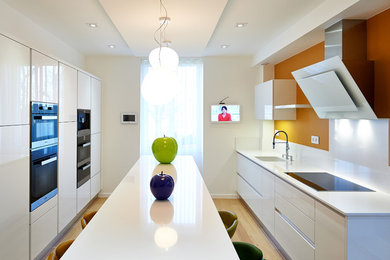 Contemporary galley kitchen in Angers with a submerged sink, flat-panel cabinets, white cabinets, yellow splashback, black appliances, light hardwood flooring, an island, brown floors and white worktops.