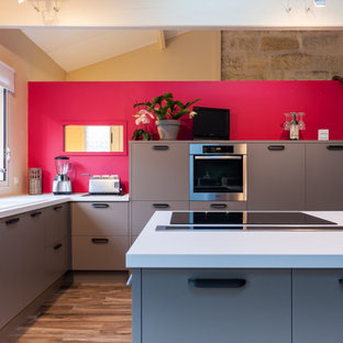 Idées déco pour une grand cuisine américaine contemporaine en L avec un plan de travail en surface solide, un îlot central, un sol marron, un plan de travail blanc, un évier encastré, un placard à porte affleurante, des portes de placard grises, un électroménager encastrable, un sol en carrelage de céramique et un plafond en poutres apparentes.