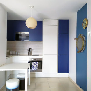 Cette image montre une cuisine marine en U avec un placard à porte plane, des portes de placard bleues, une crédence beige, un électroménager en acier inoxydable, une péninsule, un sol beige et un plan de travail blanc.
