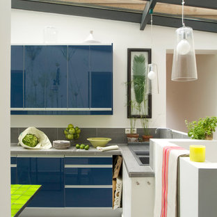 Cette image montre une cuisine américaine design en L de taille moyenne avec un placard à porte plane, des portes de placard bleues, une crédence grise et un îlot central.