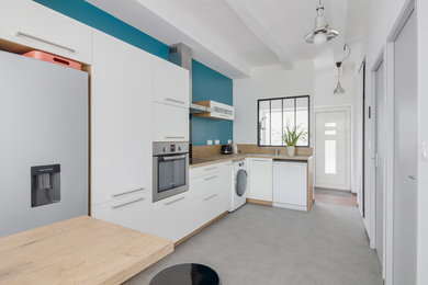 Cette photo montre une cuisine tendance en L avec un placard à porte plane, des portes de placard blanches, une crédence bleue, sol en béton ciré, un sol gris et un plan de travail beige.