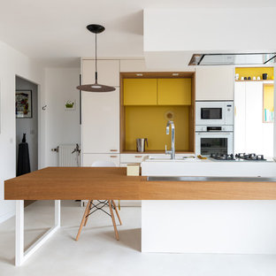 Idée de décoration pour une cuisine américaine parallèle design de taille moyenne avec des portes de placard blanches, un plan de travail en bois, une crédence jaune, un électroménager blanc, béton au sol, une péninsule, un sol blanc, un plan de travail blanc et un placard à porte plane.