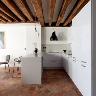 Idée de décoration pour une cuisine américaine méditerranéenne en U de taille moyenne avec un placard à porte affleurante, des portes de placard blanches, un plan de travail en quartz modifié, un sol en carreau de terre cuite, un îlot central, un sol rouge, un évier encastré, une crédence blanche, une crédence en marbre, un électroménager noir et un plan de travail blanc.