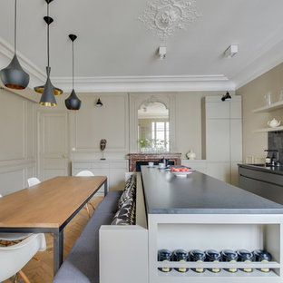 Idée de décoration pour une cuisine américaine parallèle tradition avec un placard à porte plane, des portes de placard grises, une crédence noire, un électroménager noir, un sol en bois clair, un îlot central et une crédence en carreau de terre cuite.