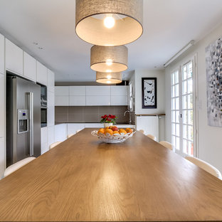 Exemple d'une grand cuisine américaine tendance en L avec un placard à porte plane, des portes de placard blanches, une crédence grise et un électroménager en acier inoxydable.
