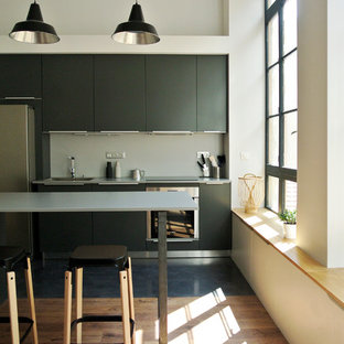 Exemple d'une cuisine américaine linéaire tendance de taille moyenne avec un placard à porte plane, des portes de placard noires, un électroménager en acier inoxydable, un sol en bois brun, un îlot central et une crédence grise.
