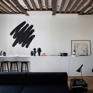 Idée de décoration pour une cuisine ouverte linéaire design avec des portes de placard blanches, une crédence blanche, un sol en bois brun, un sol marron, un plan de travail blanc, un évier encastré, un placard à porte plane, aucun îlot, un plafond à caissons et un plafond en poutres apparentes.