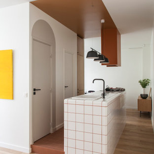 Cette image montre une cuisine nordique avec un évier posé, un plan de travail en carrelage, un sol en bois clair, un îlot central, un sol beige et un plan de travail blanc.