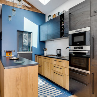 Idées déco pour une cuisine parallèle industrielle avec un évier posé, un placard à porte plane, des portes de placard en bois clair, un électroménager en acier inoxydable, une péninsule, un sol bleu et un plan de travail noir.