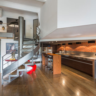 Inspiration pour une cuisine ouverte urbaine avec un évier intégré, un placard à porte plane, des portes de placard marrons, un plan de travail en inox, une crédence rouge, une crédence en brique, un électroménager en acier inoxydable, un sol en bois foncé, un îlot central et un sol marron.