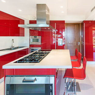 Cette image montre une cuisine design en U fermée avec un évier 2 bacs, un placard à porte plane, des portes de placard rouges, un électroménager en acier inoxydable, un îlot central et un sol blanc.