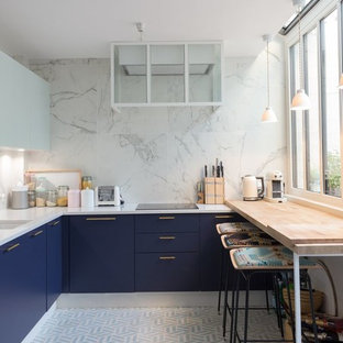 Inspiration pour une cuisine américaine design en U avec un évier encastré, un placard à porte plane, des portes de placard bleues, une crédence blanche et un sol blanc.