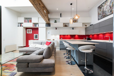 Modern inredning av ett vit vitt kök, med en undermonterad diskho, släta luckor, grå skåp, rött stänkskydd, glaspanel som stänkskydd, en köksö och svart golv