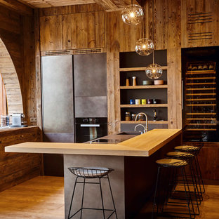 Mid-sized country l-shaped open plan kitchen in Lyon with an integrated sink, beaded inset cabinets, grey cabinets, black appliances, light hardwood floors, with island and wood benchtops.