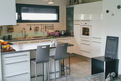 Foto de cocinas en U contemporáneo de tamaño medio abierto con encimera de laminado, salpicadero blanco, salpicadero con efecto espejo, electrodomésticos blancos, encimeras grises y suelo gris