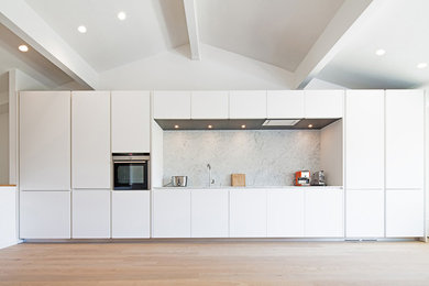 Cette photo montre une grande cuisine ouverte linéaire tendance avec un placard à porte affleurante, des portes de placard blanches, plan de travail en marbre, une crédence blanche et un électroménager blanc.
