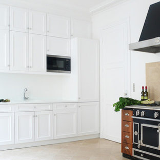 Idée de décoration pour une grand cuisine tradition en L fermée avec un évier intégré, un placard à porte affleurante, des portes de placard blanches, une crédence beige, un électroménager noir, un sol en travertin et une crédence en carreau de céramique.