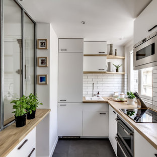 Cette image montre une cuisine nordique en U fermée et de taille moyenne avec un évier posé, un placard à porte plane, des portes de placard blanches, un plan de travail en bois, une crédence blanche, une crédence en carrelage métro, un électroménager encastrable, un sol en ardoise et aucun îlot.