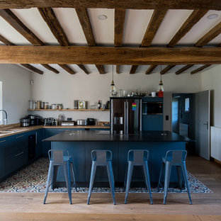 Inspiration pour une cuisine rustique en L avec un placard à porte plane, des portes de placard bleues, un plan de travail en bois, un électroménager noir, un îlot central, un sol multicolore et un plan de travail marron.