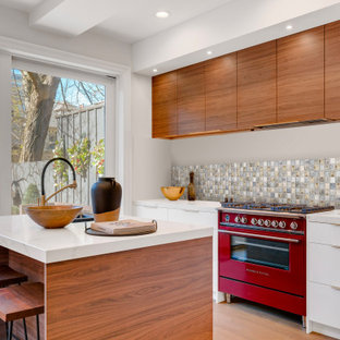 Réalisation d'une cuisine design avec un placard à porte plane, des portes de placard blanches, une crédence multicolore, une crédence en mosaïque, un électroménager de couleur, un sol en bois clair, un îlot central, un sol beige et un plan de travail blanc.