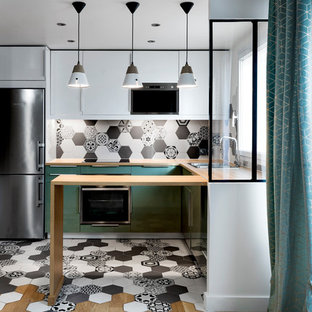 Cette photo montre une cuisine américaine méditerranéenne en U de taille moyenne avec un évier posé, un placard à porte plane, des portes de placard blanches, un plan de travail en bois, une crédence multicolore, une crédence en carreau de ciment, un sol en carreaux de ciment, un sol multicolore et un plan de travail beige.