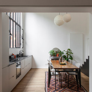Idée de décoration pour une cuisine américaine linéaire design avec un évier encastré, un placard à porte plane, des portes de placard grises, un sol en bois clair, un sol beige et un plan de travail noir.